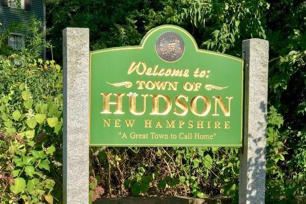 Light green wood sign with words Welcome to Town of Hudson New Hampshire
