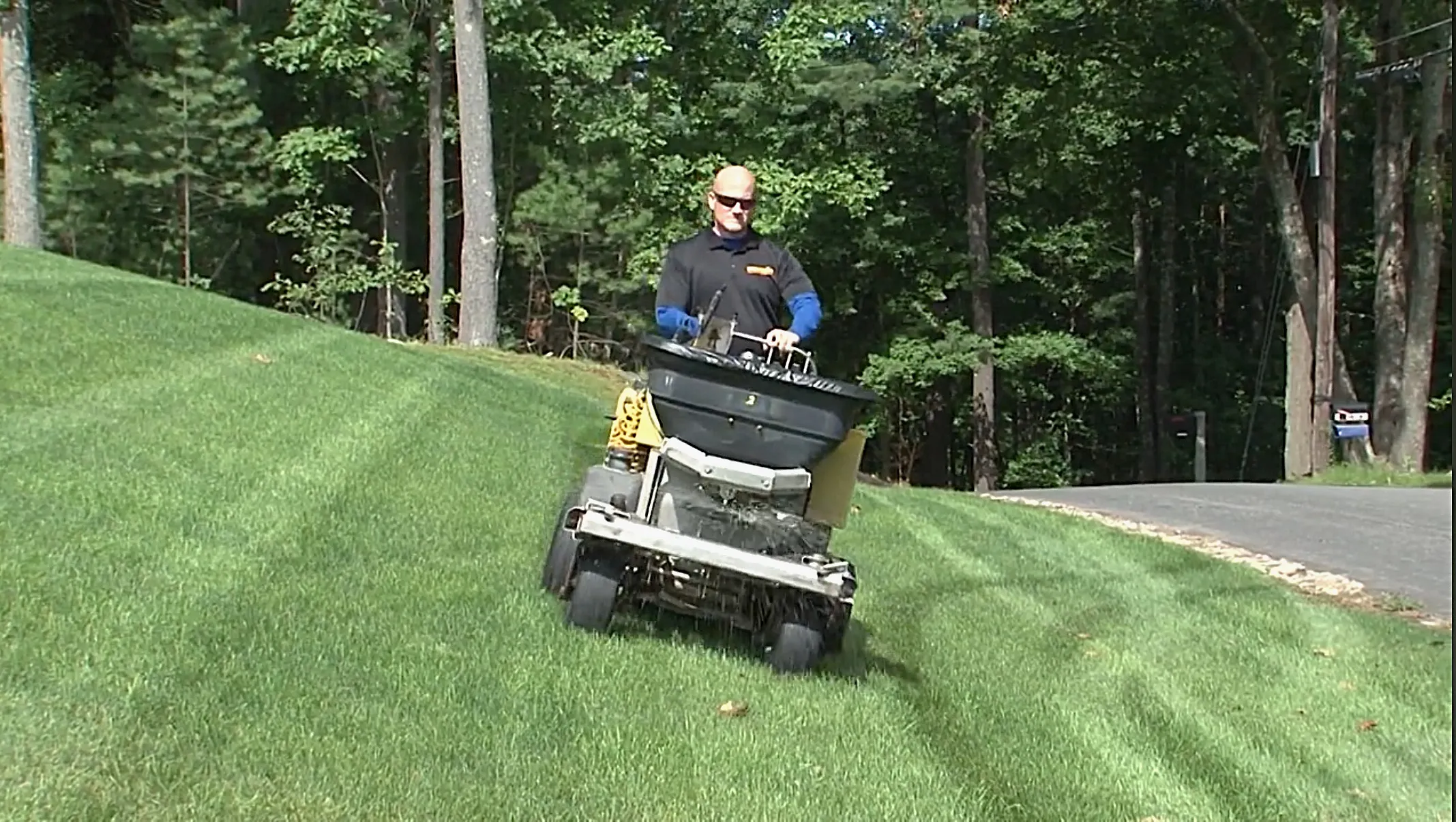 Professional lawn care technician operating a spreader on a lush green lawn, emphasizing effective pest management and turf health in Derry, New Hampshire.