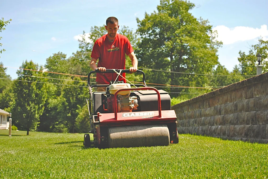 Groundhog Turf Care technician mowing lawn with roller, Derry, NH